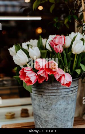 Tulipes roses et blanches fraîches disposées dans un seau en métal rustique. Les fleurs de printemps créent une composition florale lumineuse et confortable avec une lumière naturelle et un cha Banque D'Images