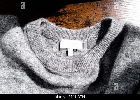 Pull tricoté gris doux avec étiquette de vêtement vierge sur une surface en bois. Concept de mode minimaliste confortable mettant en valeur la texture, la chaleur et le style décontracté Banque D'Images