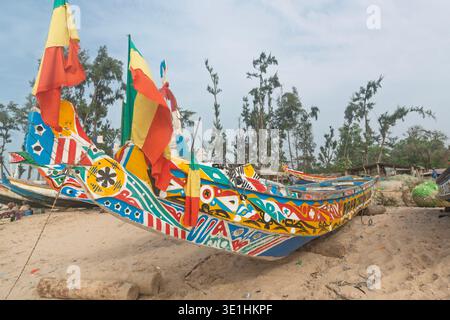 Vue de face d'un bateau de pêche traditionnel en bois (pirogue) avec drapeaux nationaux sur la proue sur la plage d'Abéné, Casamance, Sénégal. Banque D'Images