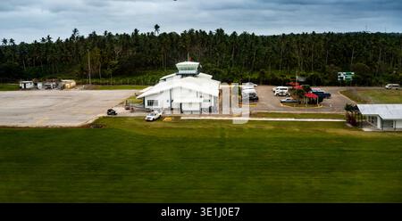 Une vue aérienne d'un petit terminal d'aéroport avec une tour de contrôle, entouré de palmiers luxuriants. Plusieurs véhicules, dont un pick-up blanc tr Banque D'Images