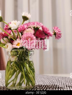 Délicates fleurs roses et blanches disposées dans un simple bocal en verre créant une charmante décoration de table. La scène intérieure naturelle illustre le moderne Banque D'Images
