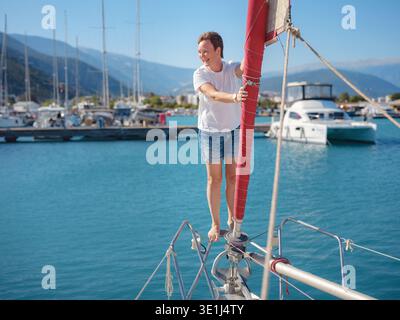 Femme marin tient le tissu de voile blanc se préparant à lever des voiles sur le yacht. L'activité physique et les compétences de maniement de bateau sont montrées pendant la préparation pour le voyage en voilier près de la côte de Finike. Banque D'Images