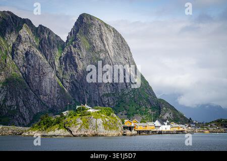 Village de pêcheurs côtier avec des maisons en bois sur pilotis sous la montagne rocheuse escarpée à côté de la mer calme Banque D'Images