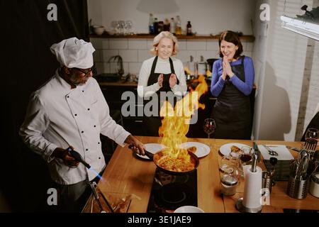 Homme d'âge moyen enseignant le cours de cuisine démontrant la technique du flambe Banque D'Images
