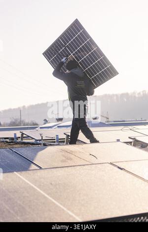 Un ouvrier installe un panneau solaire sur un toit à la lumière du matin, montage PV à OBI Baumarkt, Muehlacker, Enzkreis, Allemagne Banque D'Images