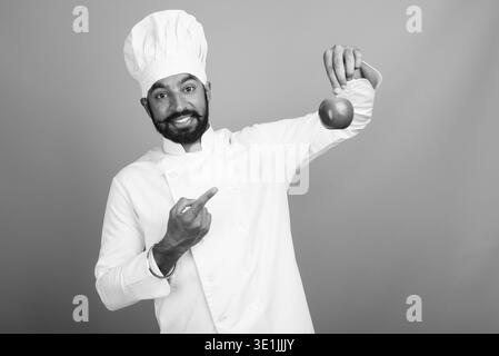 Studio shot du jeune bel homme indien barbu en tant que chef sur fond gris en noir et blanc Banque D'Images