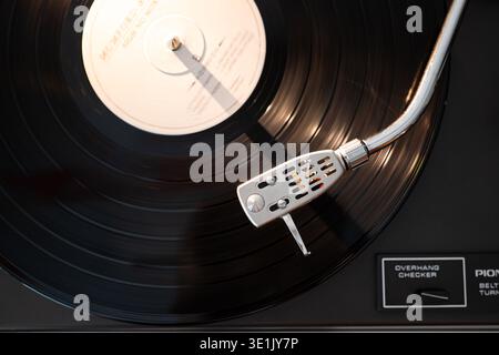 Gros plan d'un disque vinyle sur une platine, avec une tonalité argentée et un stylet, avec des rainures visibles et l'étiquette de disque au centre Banque D'Images