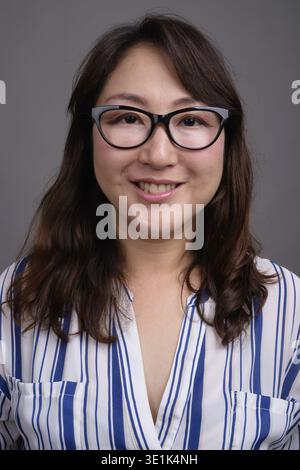 Studio shot of mature belle asiatique businesswoman wearing eyeglasses contre l'arrière-plan gris Banque D'Images