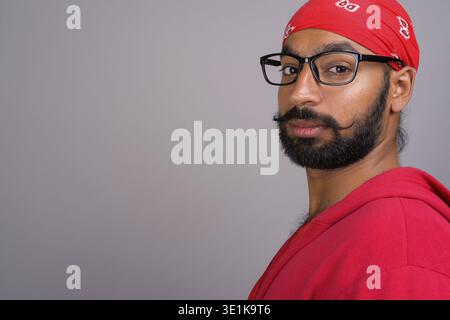 Studio shot of young handsome Indian man wearing eyeglasses contre l'arrière-plan gris Banque D'Images