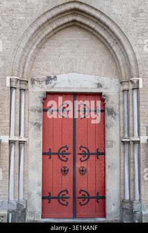 Zutphen, Gueldre, pays-Bas, porte en bois rouge ornée avec des détails en fer noir sous une arche en pierre et un mur de briques Banque D'Images
