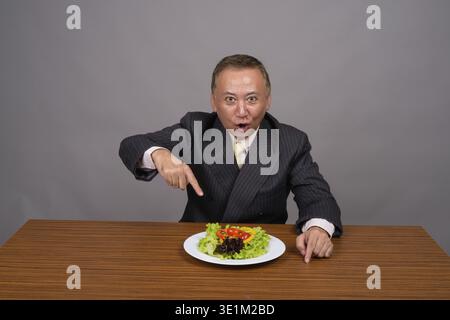 Studio tourné d'un homme d'affaires asiatique mûr assis avec une table en bois sur fond gris Banque D'Images