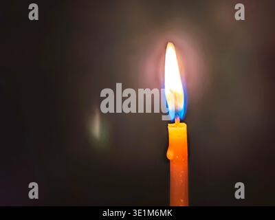 Une bougie brûle dans le monastère Athos de Michael à Adygea, Russie. La flamme éclaire la zone, montrant la lueur chaude autour de la bougie contre le d. Banque D'Images