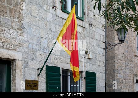 Gros plan du drapeau monténégrin rouge et or affiché sur la façade d'une maison de maçonnerie méditerranéenne traditionnelle dans la vieille ville protégée par l'UNESCO. Banque D'Images