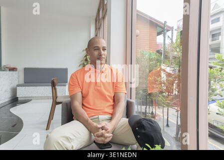 Beau visage d'homme chauve italien d'âge moyen dans un polo orange assis à la table du café. Concept de style de vie décontracté Banque D'Images