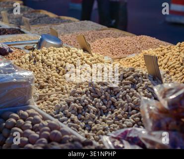 Étalage de marché avec assortiment de légumineuses séchées et de noix dans des bacs ouverts, avec des pelles et des étiquettes, faible profondeur de champ, lumière naturelle chaude. Banque D'Images