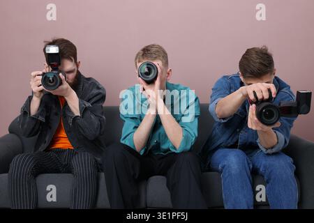 Groupe de photographes prenant des photos avec des appareils photo professionnels sur canapé sur fond de couleur Banque D'Images