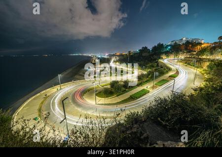 Spectaculaire photographie nocturne longue exposition d'une route côtière sinueuse avec des traînées de lumière rouge et blanche éclatantes provenant des voitures qui passent. La route embrasse le rocher Banque D'Images