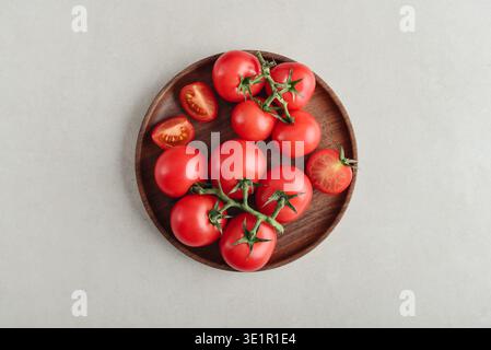 Une branche de tomates cocktail roses sur assiette en bois sur fond clair, vue de dessus Banque D'Images