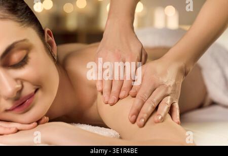 Femme détendue recevant un massage des épaules dans le spa avec une ambiance chaleureuse aux chandelles Banque D'Images