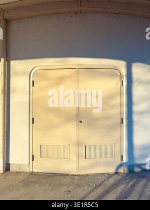 Deux portes sont installées dans un mur lumineux. Le soleil est bas, faisant de longues ombres sur le sol. La scène montre une zone simple sans personne autour. Banque D'Images