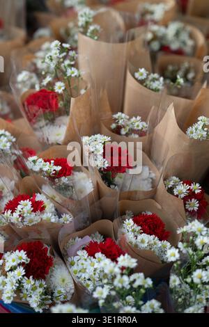 Gros plan de petits bouquets de fleurs mélangées avec des marguerites blanches et des œillets rouges enveloppés dans du papier kraft brun. Arrangements floraux frais affichés à un l Banque D'Images