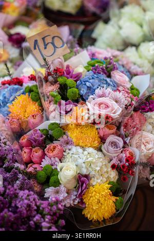 Bouquets de fleurs mélangées vibrantes exposés à la vente sur un marché avec une étiquette de prix visible. Arrangement coloré de roses, hortensias et chrysanthèmes Banque D'Images