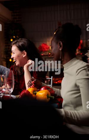 Femme joyeuse s'amusant sur les vacances de Noël, se réunissant avec le groupe d'amis à la table de dîner et appréciant la bonne nourriture. Joyeuse personne festive s'amusant avec les gens à la maison, boire du vin. Banque D'Images