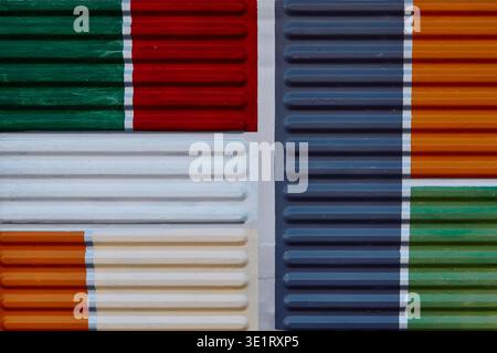 Texture de revêtement métallique nervuré multicolore avec des sections de rouge, vert, orange, bleu et blanc disposées dans un dessin géométrique sur un mur Banque D'Images
