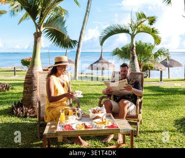 Couple savourant un délicieux petit déjeuner gastronomique entouré de palmiers, avec l'océan turquoise magnifique en arrière-plan. Une façon parfaite de commencer la journée au paradis à Maurice Banque D'Images