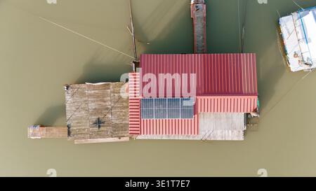 Vue aérienne d'une maison flottante avec un toit rouge et des panneaux solaires repose doucement sur l'eau trouble, Novi Sad, Voïvodine, Serbie. Banque D'Images