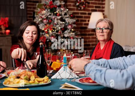 Grand-mère au dîner de saison avec la famille profitant des vacances de noël à la maison décoré avec des ornements de fête et arbre de Noël. Femme senior rencontrant des parents et des amis autour de la table. Banque D'Images