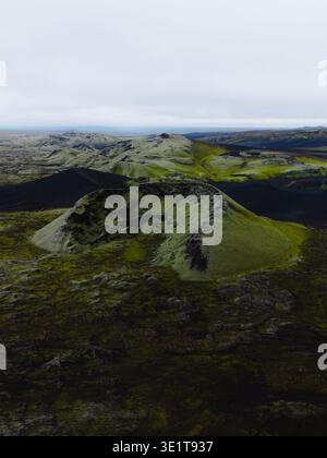 Vue aérienne des cônes volcaniques couverts de mousse s'élèvent de façon spectaculaire du paysage sombre sous un ciel brumeux, Lakagigar, Islande. Banque D'Images