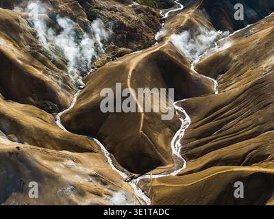 Vue aérienne des rivières glaciaires sinueuses creusant à travers le paysage volcanique, avec de la vapeur s'élevant des évents géothermiques, Landmannalaugar, Islande. Banque D'Images