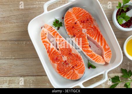 steaks de saumon crus sur plaque blanche, fond en bois, vue de dessus Banque D'Images
