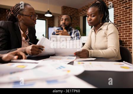 Entrepreneurs afro-américains avec des documents discutant et consultant autour de la table de réunion dans le bureau de mur de brique. L'équipe de démarrage planifie le projet d'entreprise ensemble et travaille à un accord. Banque D'Images