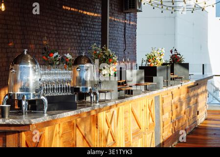 Bar extérieur élégant sur le toit-terrasse avec un long comptoir en marbre, de nombreux plats argentés, des flûtes à champagne, des fleurs éclatantes Banque D'Images