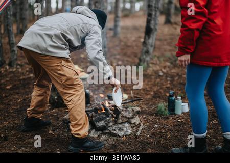 Couple cuisinant sur un feu de camp dans une forêt de pins pendant un voyage de camping extérieur frais Banque D'Images