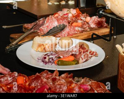 Assiette de charcuterie avec assortiment de charcuteries, pain et cornichons servis en apéritif sur une table de buffet pour la restauration ou les événements festifs. Banque D'Images
