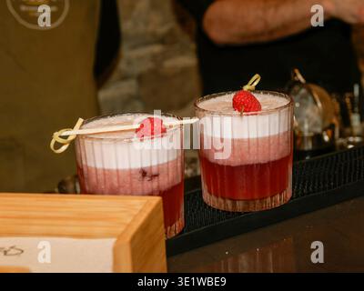 Gros plan de deux élégants cocktails de framboises servis dans des verres sur un comptoir de bar, surmontés de framboises fraîches et de mousse Banque D'Images