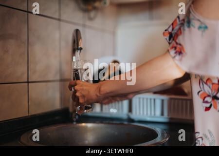 Femme remplissant un verre avec de l'eau d'un robinet de cuisine au-dessus de l'évier Banque D'Images