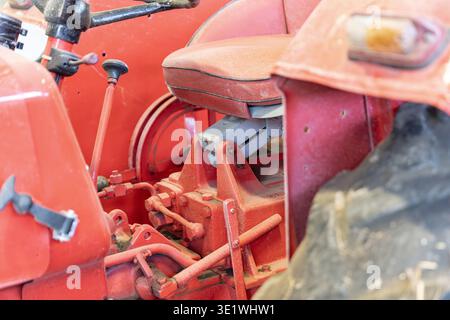 Un gros plan présente les détails d'un tracteur vintage rouge, y compris le volant de siège et divers composants mécaniques transpo agricole Banque D'Images