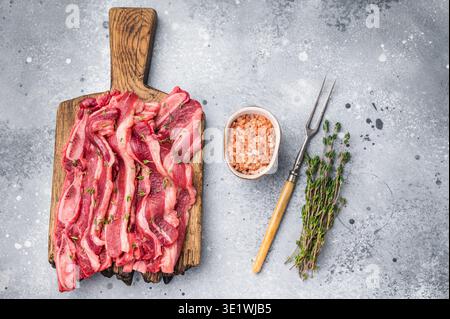 Lanières de viande de côtes courtes crues de qualité supérieure assaisonnées de sel et de thym, présentées sur une planche de bois Banque D'Images