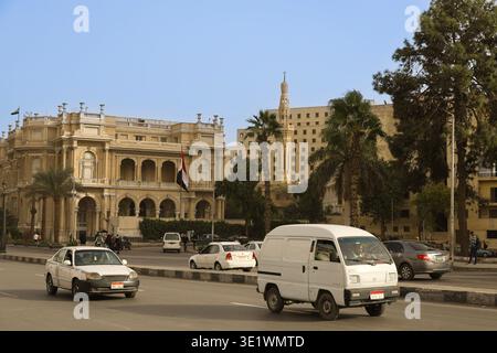 Scène de circulation sur un pont du Nil au Caire, en Égypte, avec des voitures se déplaçant le long d'une large route bordée de palmiers et de grands bâtiments historiques avec cla Banque D'Images