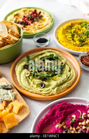Une planche de charcuterie vibrante présente du brocoli, du curcuma, du houmous classique et de la betterave, associés à des olives, craquelins, et garnitures fraîches, parfait pour Banque D'Images
