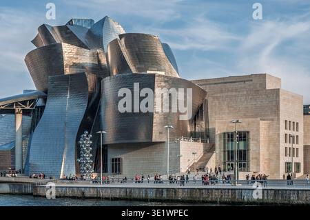 Le musée Guggenheim Bilbao, conçu par Frank Gehry, présente ses courbes emblématiques revêtues de titane sous un ciel bleu vif près de la rivière Nervion. Espagne. Banque D'Images