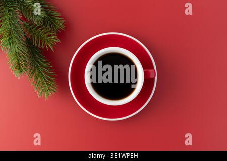 Tasse blanche rouge de café noir chaud fraîchement infusé avec décor de branche d'arbre de Noël sur fond rouge. Banque D'Images