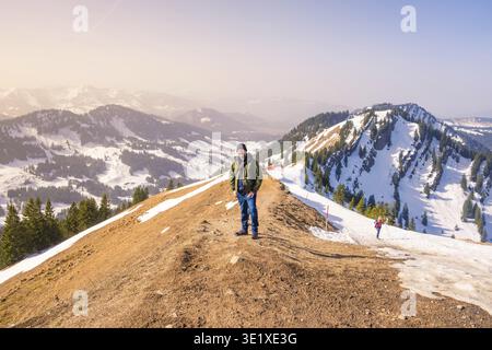 Un randonneur se tient sur une crête de montagne enneigée avec de vastes vues sur la montagne sous un ciel clair, montagnes Hochgrat, Alpes Allgaeu, Oberreute, Allemagne Banque D'Images
