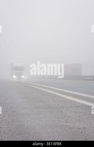 Voitures avec des feux de brouillard sur l'autoroute. Mauvais temps sur la route. Route le jour brumeux en perspective avec espace de copie. Concept de conditions de conduite. Banque D'Images