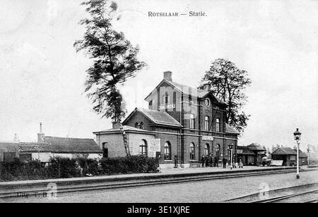 La gare de Rotselaar est une gare ferroviaire de Rotselaar, une commune du Brabant flamand, en Belgique, desservie par des lignes ferroviaires reliant Louvain, Aarschot et Wezemaal dans le réseau ferroviaire belge développé au cours du XIXe siècle. Le tirage photographique d'archives enregistre la vue intérieure de la zone de la gare avec le bâtiment de passagers, les voies et les plates-formes identifiés avec le nom Rotselaer dans un format de carte postale datant d'environ 1900. Banque D'Images
