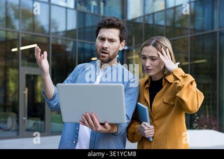 Deux gens d'affaires stressés se sentent confus et frustrés lorsqu'ils regardent un ordinateur portable à l'extérieur, rencontrant un problème ou un bug logiciel pendant leur travail Banque D'Images